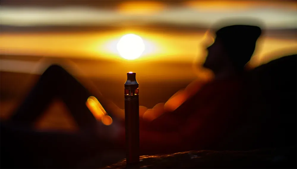 casual vaping with a buttonless disposable vape pen during a serene sunset